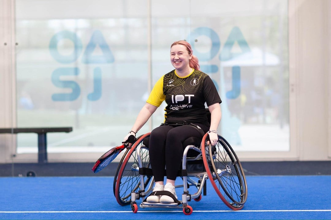 Wheelchair padel player Kristen Paskins smiling while sat in her wheelchair and holding a padel racket at the Inclusive Padel Tour